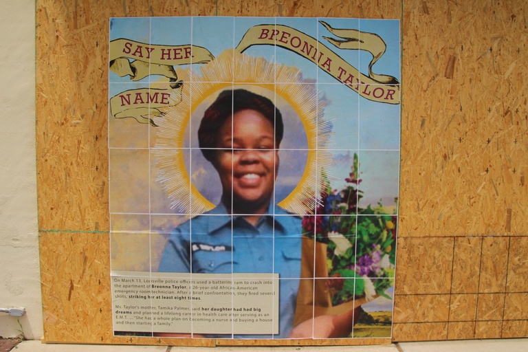 A mural displaying a photograph of Breonna Taylor with a halo around her head and the words "say her name."