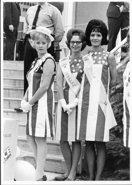 Three women in stars and stripes dresses wearing George Wallace sashes. 
