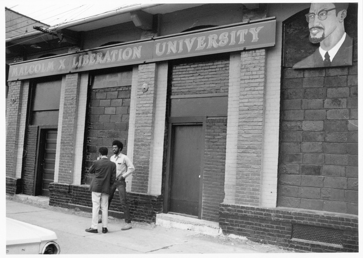 Howard Fuller and an unidentified student stand in front of a building with a sign that reads "Malcom X Liberation University."