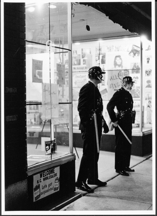 Two police officers in riot gear stand outside a storefront. 
