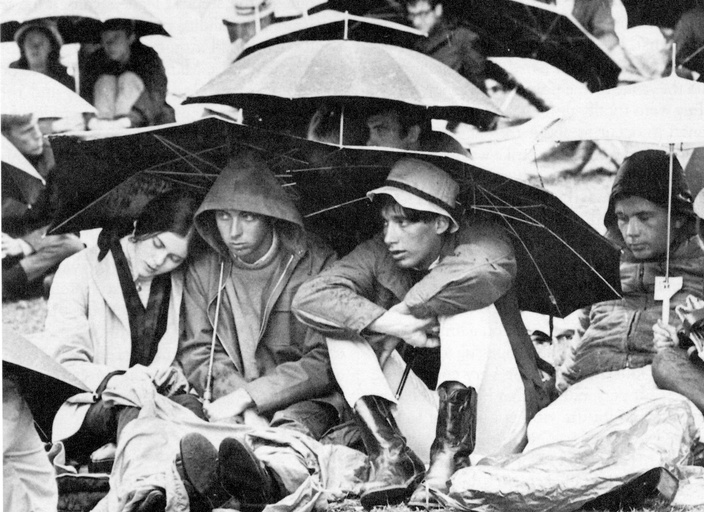 A group of people sit on the ground under umbrellas. 