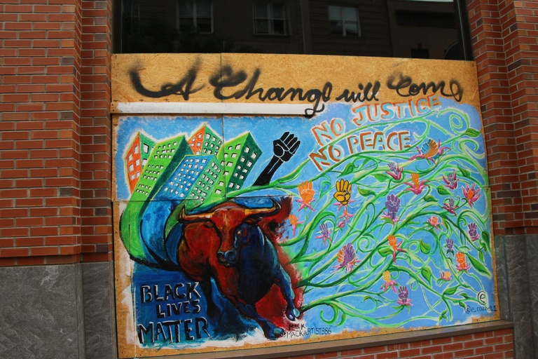 A mural with a blue background displaying buildings, raised "power" fists as flowers, a bull, and the words "Black Lives Matter," "A change will come," and "No justice no peace."