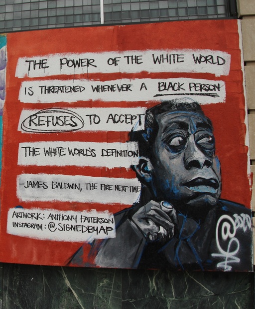 A red mural depicting James Baldwin and the words "the power of the white world is threatened whenever a black person refuses to accept the white world's definition. - James Baldwin, The Fire Next Time."