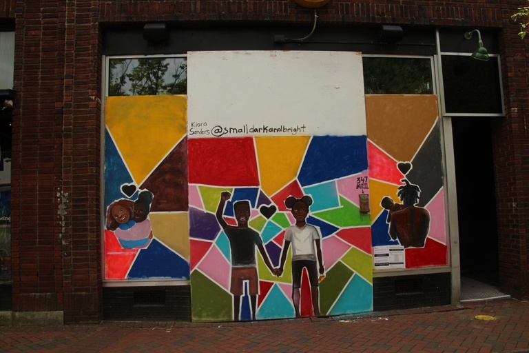 Colorful geometric shapes in the background with images of black men, women, and children embracing. 