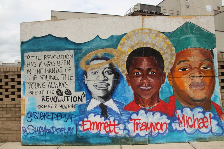 The faces of Emmett Till, Trayvon Martin, and Michael Brown as angels and the words "The revolution has always been in the hands of the young. The young always inherit the revolution. - Dr. Huey P. Newton."