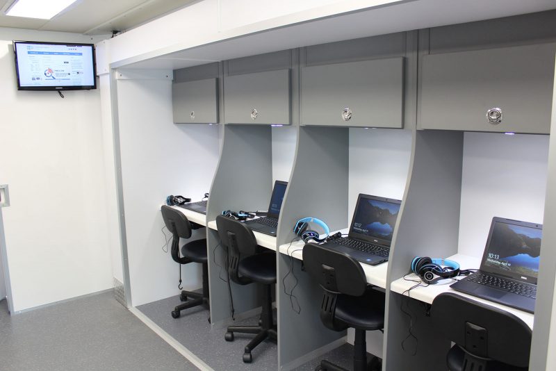 Rows of desks. each with a laptop, noise-cancelling headphones, and a storage locker above