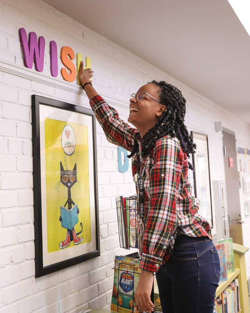 Ms. Danielle laughs while hanging up the last letter in a wall decoration saying "wish"
