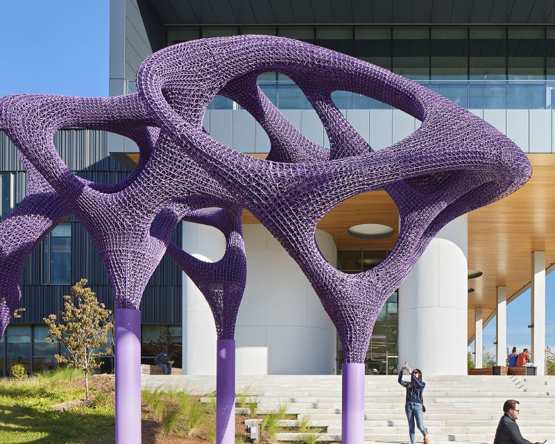 A large, purple, abstract sculpture standing in front of the building