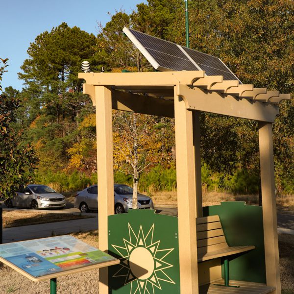 A covered bench with a solar panel on its roof and a sign with text and pictures next to it