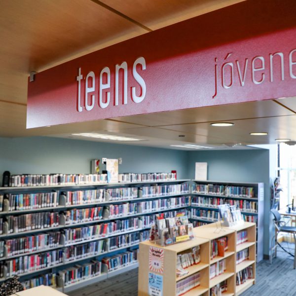 Sign sayings "teens" above an area with bookshelves, seating, and windows