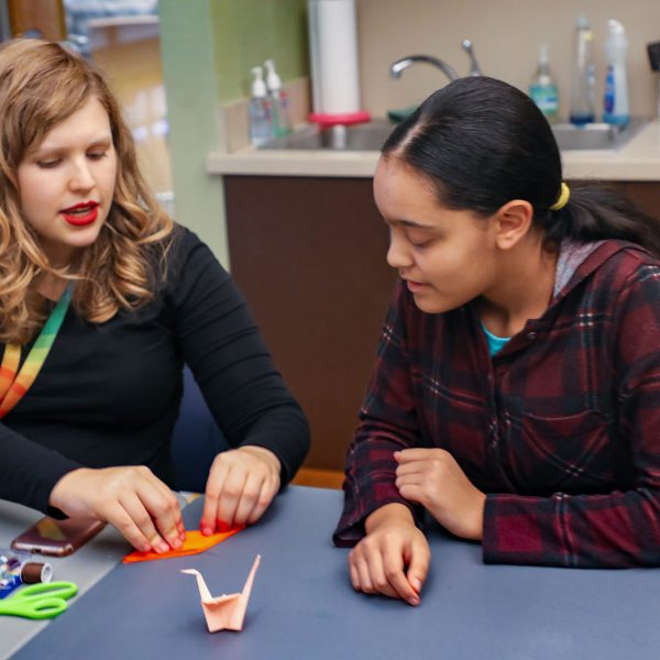 A librarian shows a teen how to fold a piece of origami paper