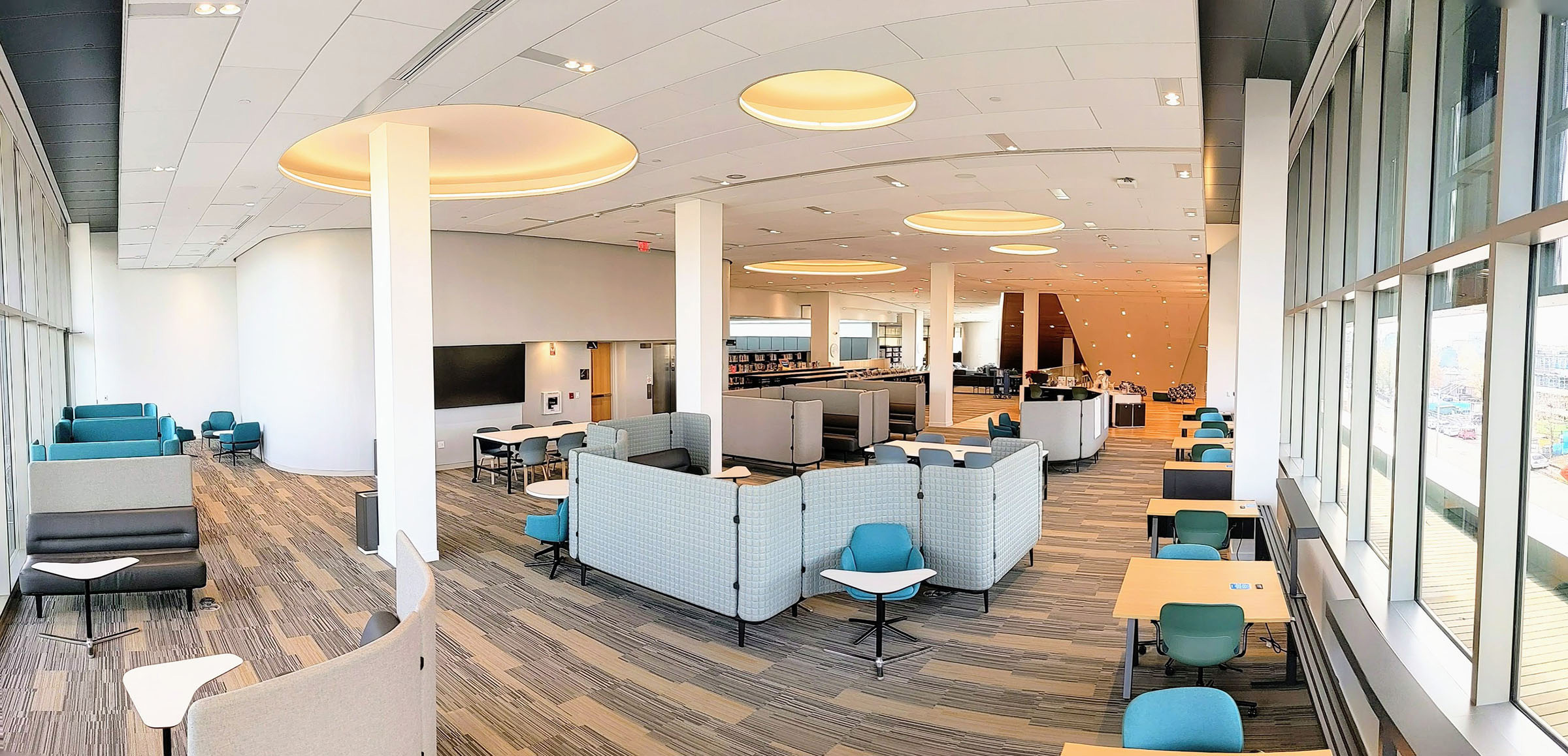 Panoramic view of the Incubator at Main Library - a large space full of seating, stretching from the wall of windows to the main staircase