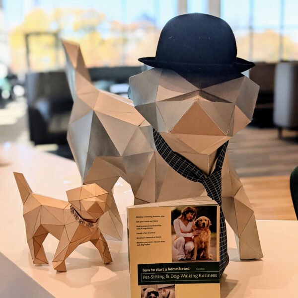 Poly the Puppy, a polygonal dog figure wearing a jaunty business hat and tie, plus baby poly puppy, pose with the book "How to Start a Home-Based Pet-Sitting and Dog-Walking Business"