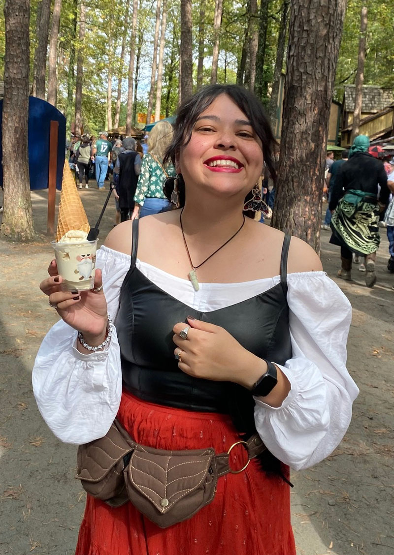 Children's librarian Ms. Elmera dressed in a Renaissance costume and holding up an ice cream cone