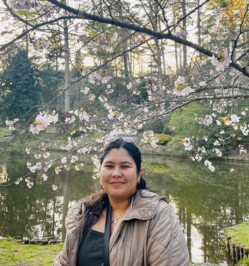 Natalia in front of a reflective pond with flowering tree branches overhead