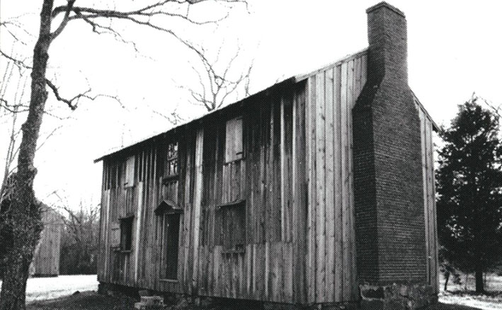 Black-and-white photograph of one of the former slave quarters in the Horton Grove area of the Stagville Plantation, a multiple-story building with shutters on the windows and a brick chimney.
